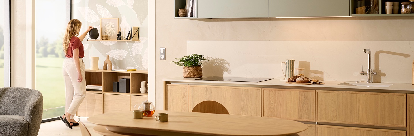 Warm natural oak kitchen and living space with a woman styling shelves